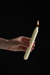 Photo of Woman holding burning candle on black background, closeup