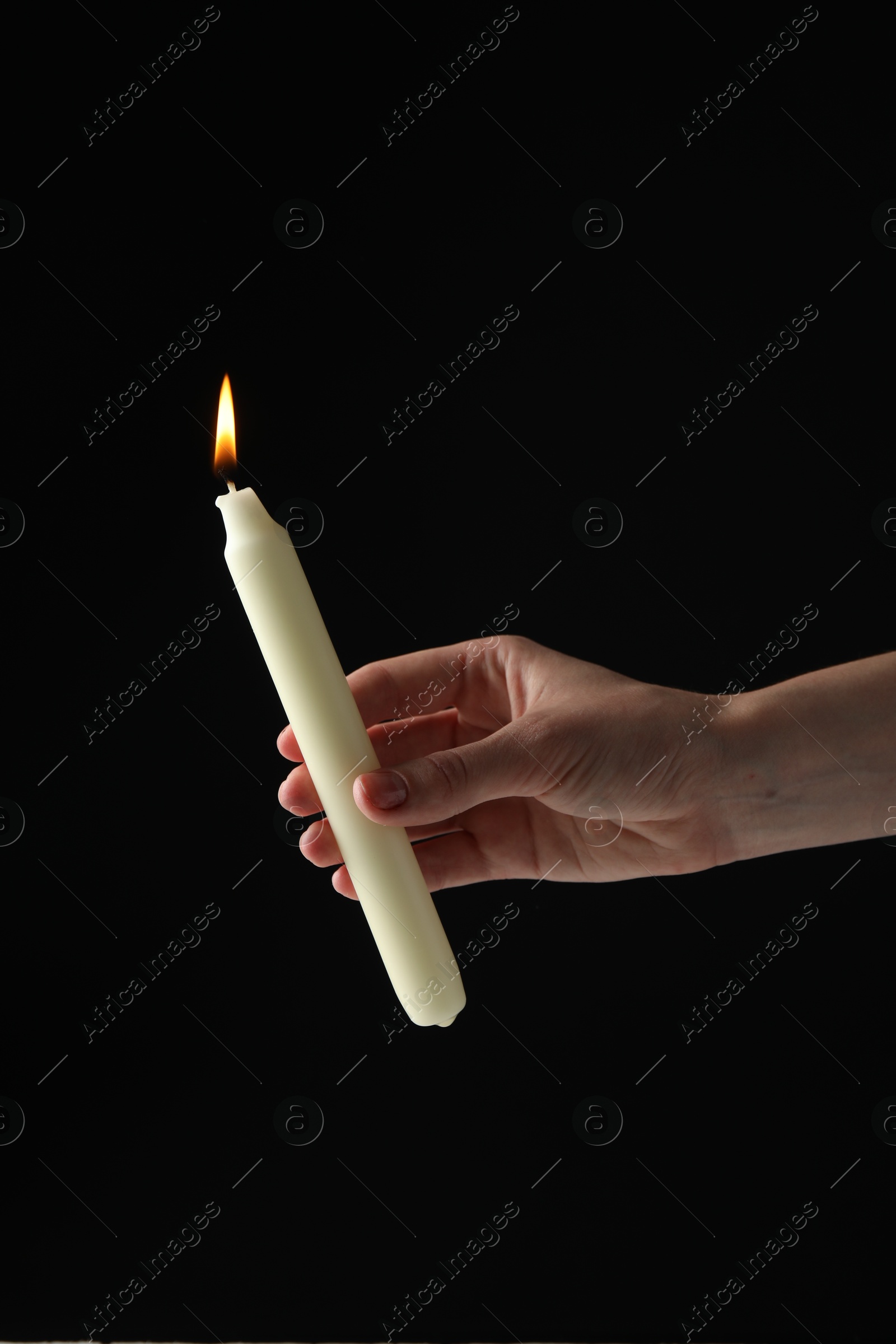 Photo of Woman holding burning candle on black background, closeup