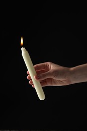 Woman holding burning candle on black background, closeup