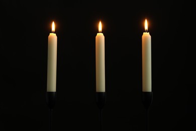 Many burning church candles on black background