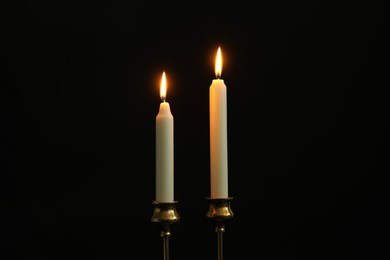 Two burning church candles on black background