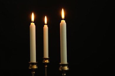 Many burning church candles on black background