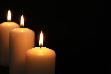 Photo of Many burning candles on black background, closeup. Space for text