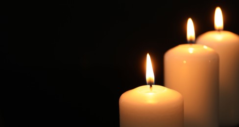 Many burning candles on black background, closeup. Space for text