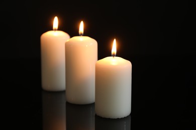 Photo of Many burning candles on mirror surface against black background