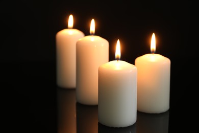 Photo of Many burning candles on mirror surface against black background