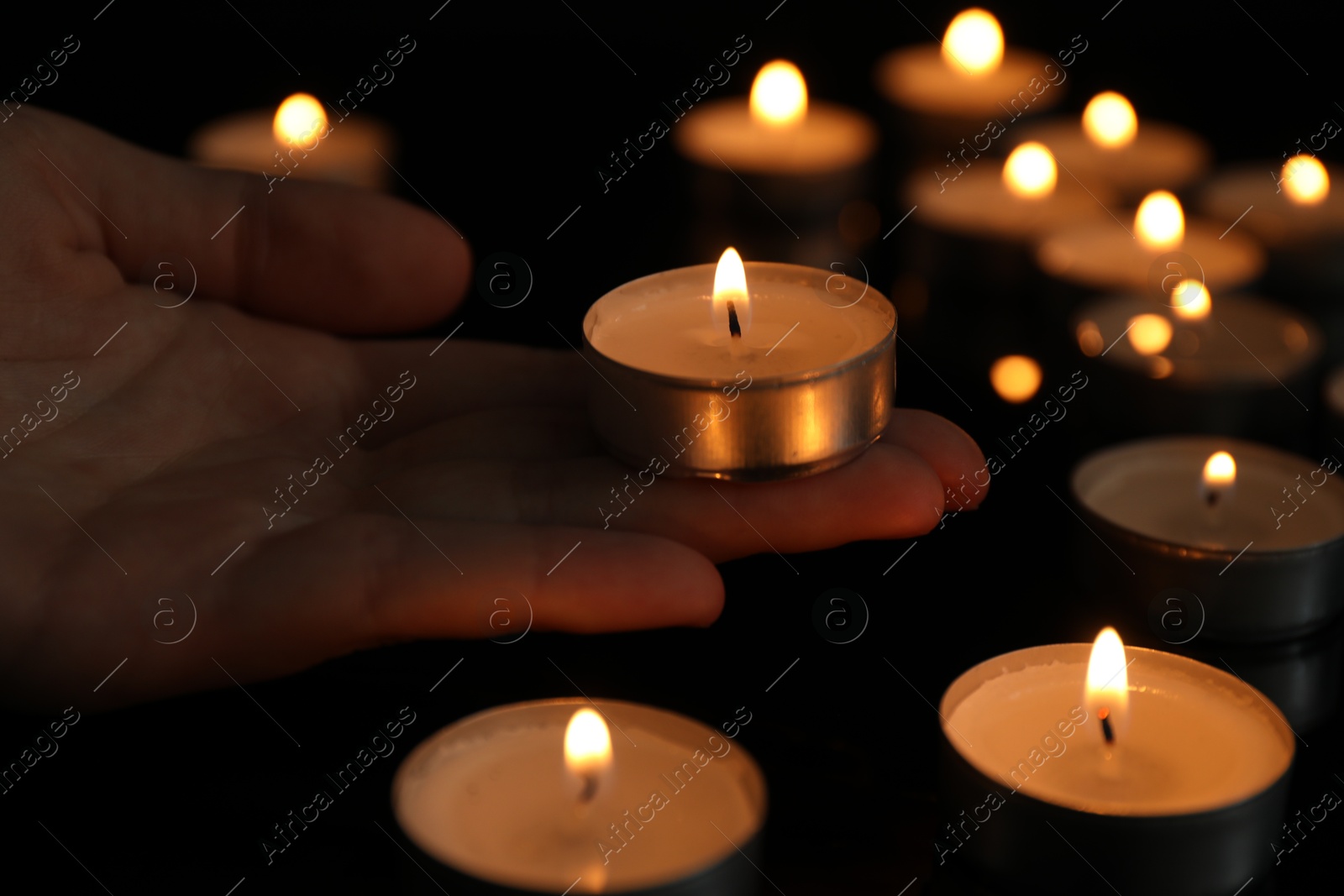 Photo of Woman holding burning tealight candle on black background, closeup