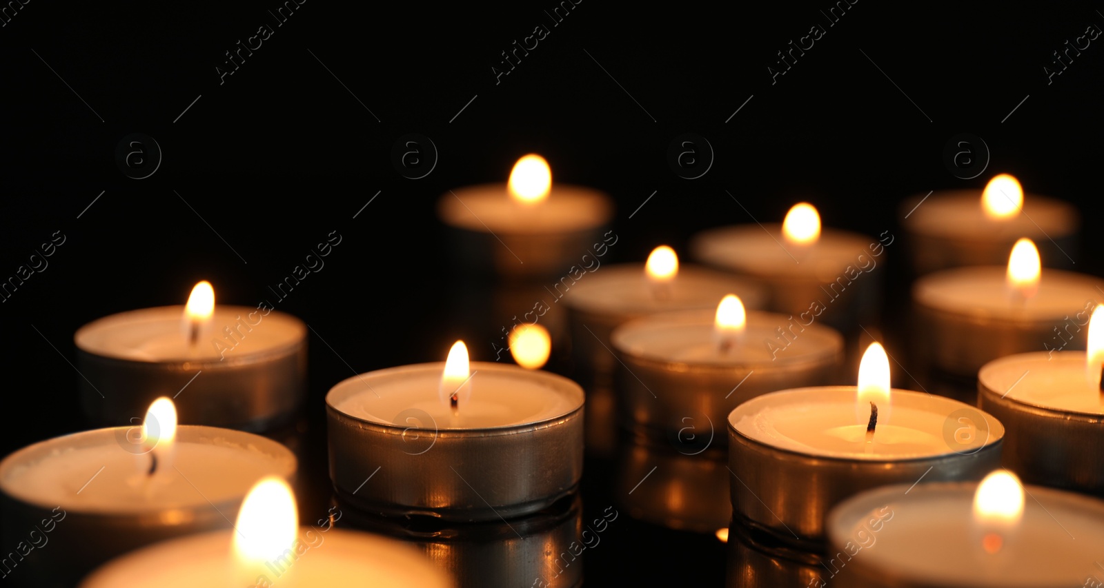 Photo of Many burning tealight candles on black background, closeup