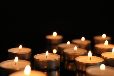 Photo of Many burning tealight candles on black background, closeup