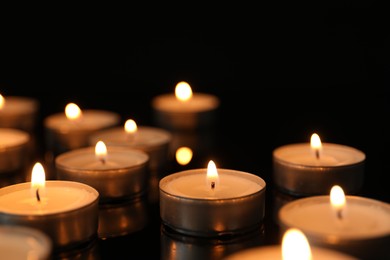 Many burning tealight candles on black background, closeup