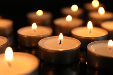 Photo of Many burning tealight candles on black background, closeup