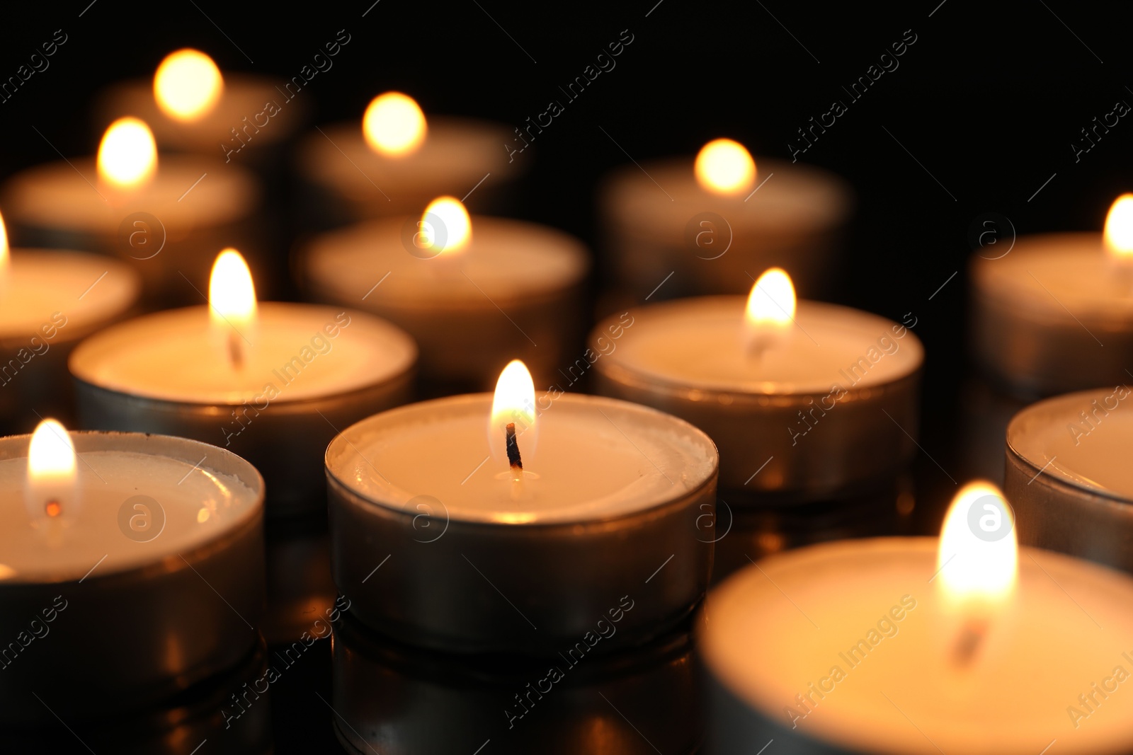 Photo of Many burning tealight candles on black background, closeup
