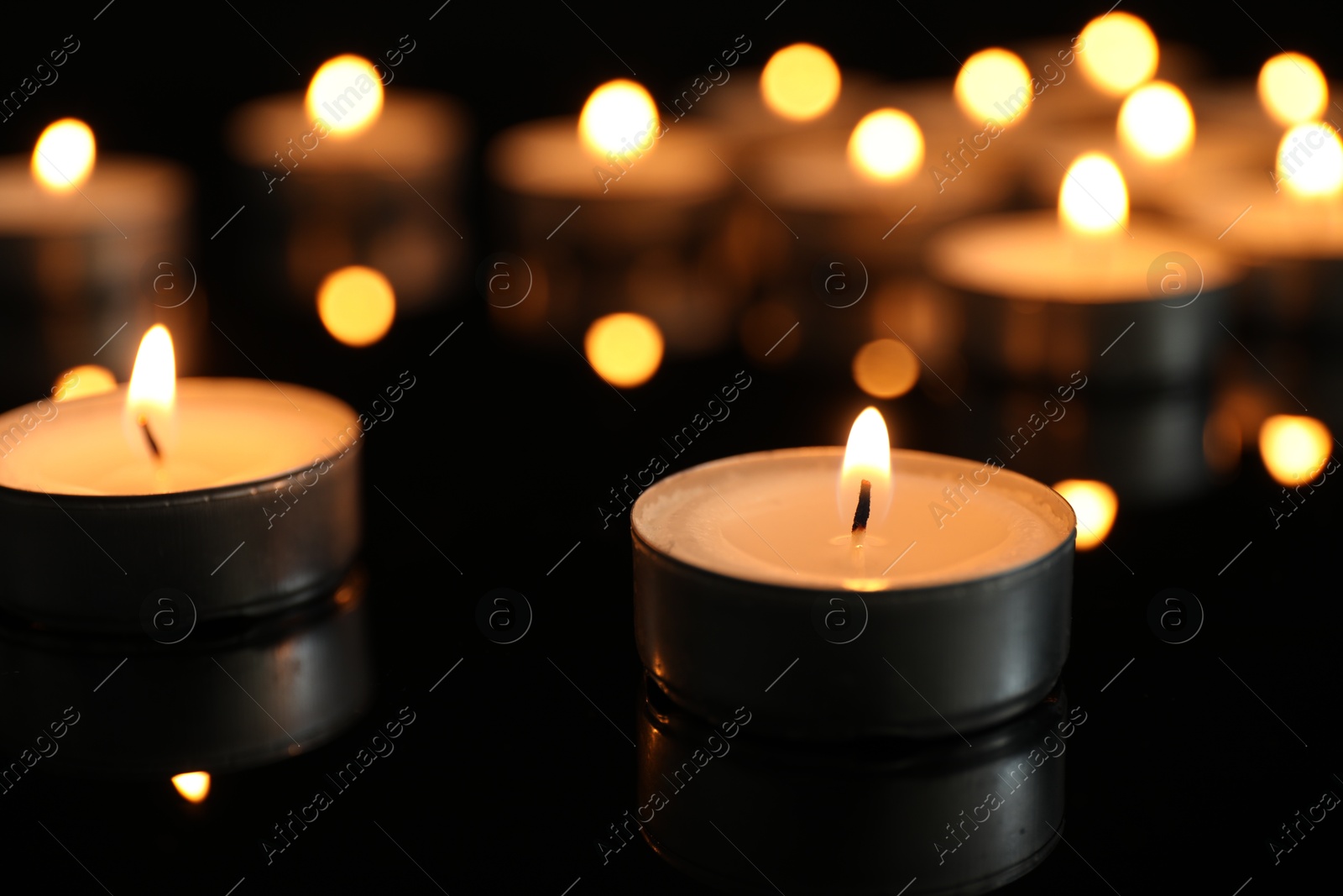 Photo of Many burning tealight candles on black background, closeup