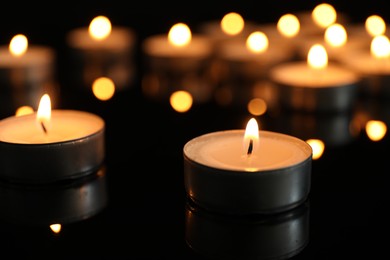 Many burning tealight candles on black background, closeup