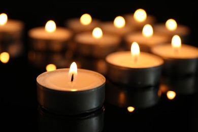 Many burning tealight candles on black background, closeup