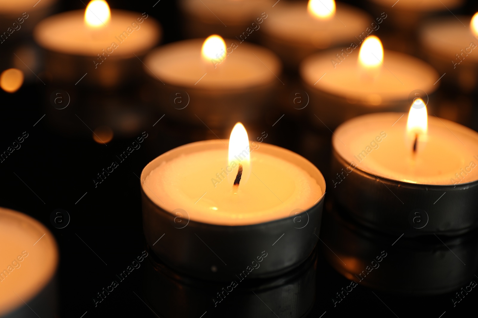 Photo of Many burning tealight candles on black background, closeup