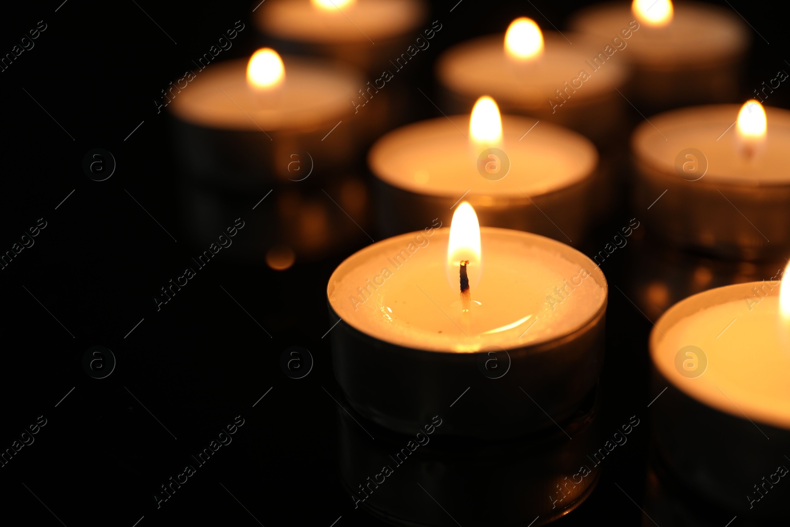 Photo of Many burning tealight candles on black background, closeup