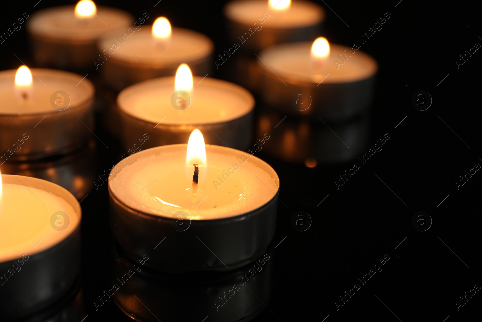 Photo of Many burning tealight candles on black background, closeup