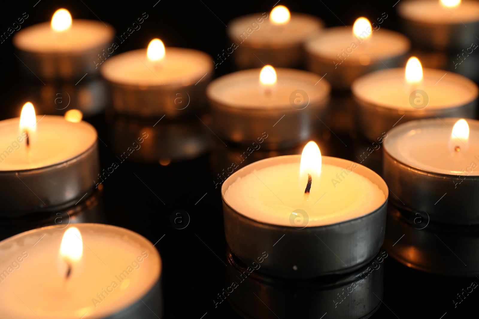 Photo of Many burning tealight candles on black background, closeup