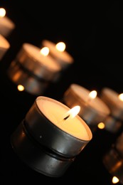 Photo of Many burning tealight candles on black background, closeup