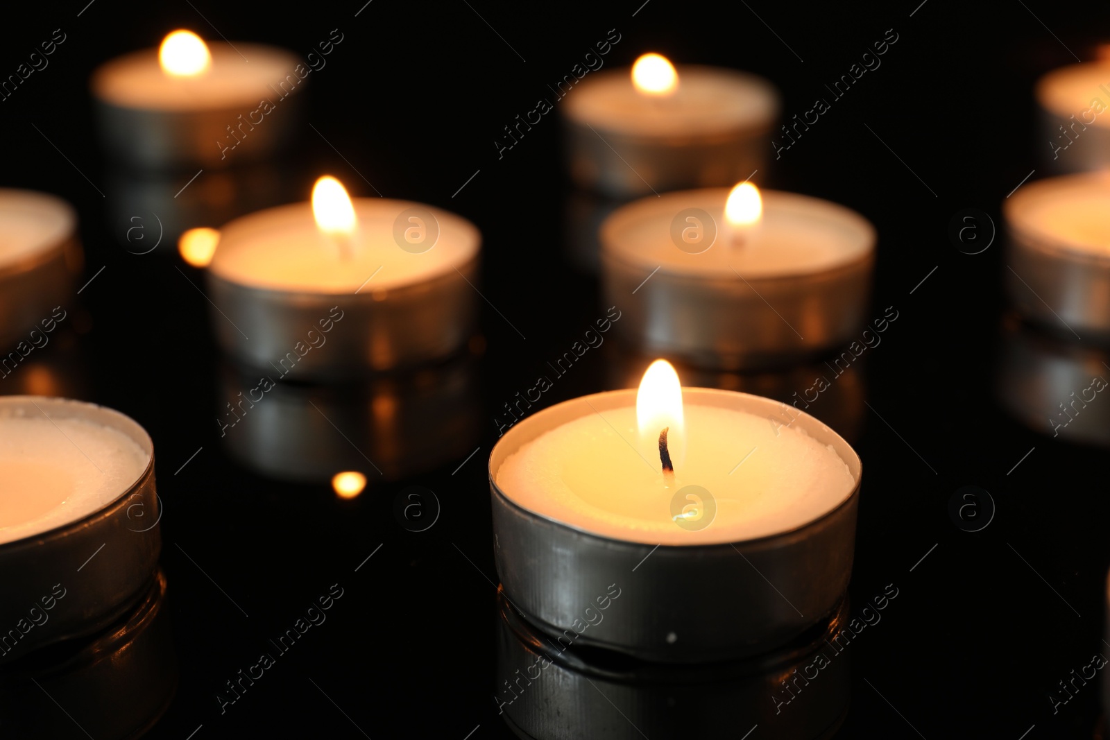 Photo of Many burning tealight candles on black background, closeup