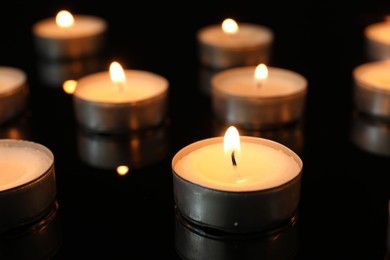 Many burning tealight candles on black background, closeup