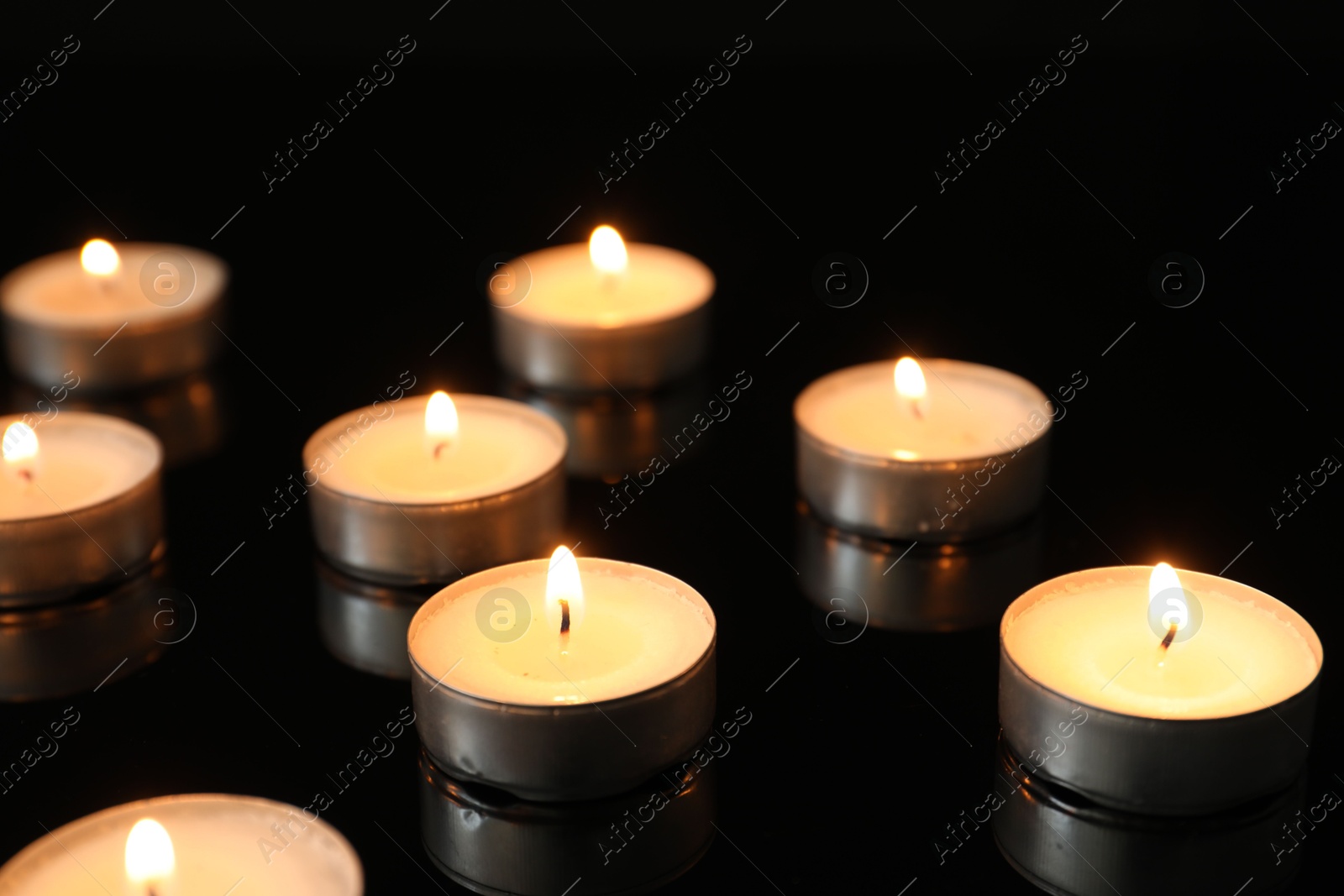 Photo of Many burning tealight candles on mirror surface against black background