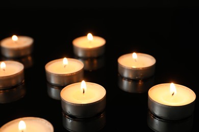 Many burning tealight candles on mirror surface against black background