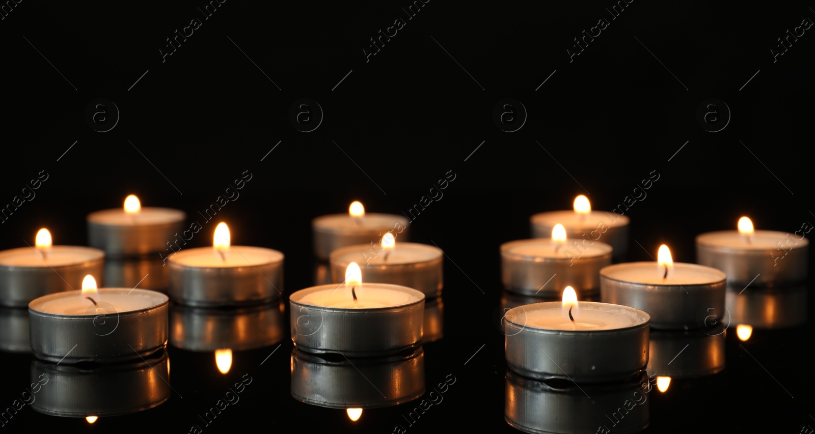 Photo of Many burning tealight candles on mirror surface against black background. Banner design