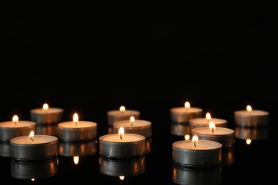 Photo of Many burning tealight candles on mirror surface against black background