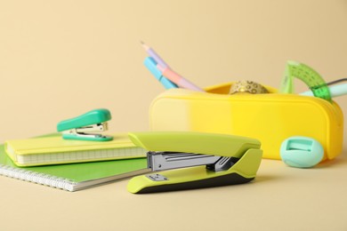 Photo of Green stapler and other stationery on beige background, closeup