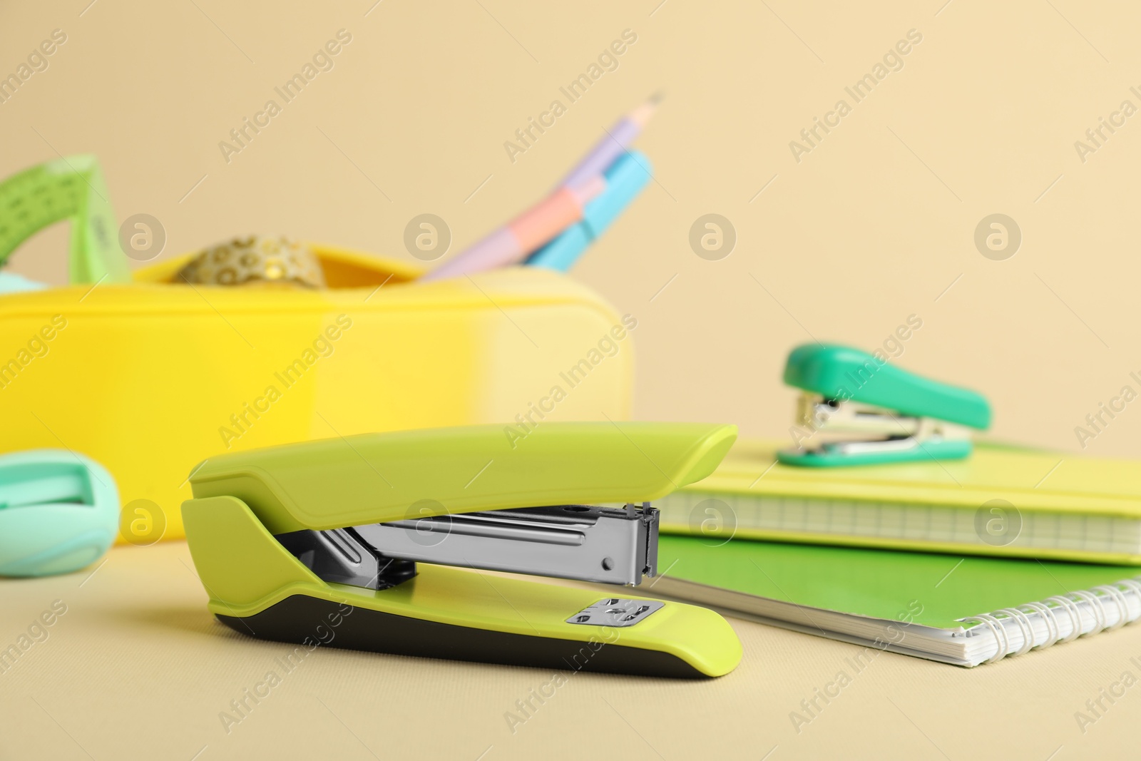 Photo of Green stapler and other stationery on beige background, closeup