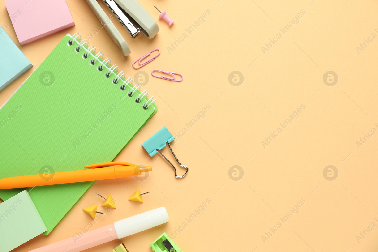 Photo of Flat lay composition with notebook, stapler and different stationery on pale orange background, space for text