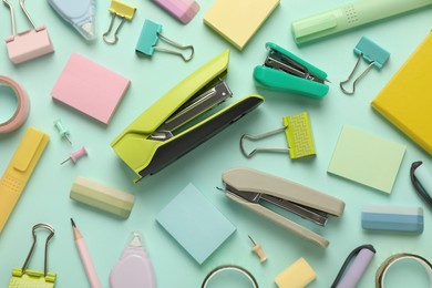 Photo of Flat lay composition with notebook, staplers and different stationery on turquoise background