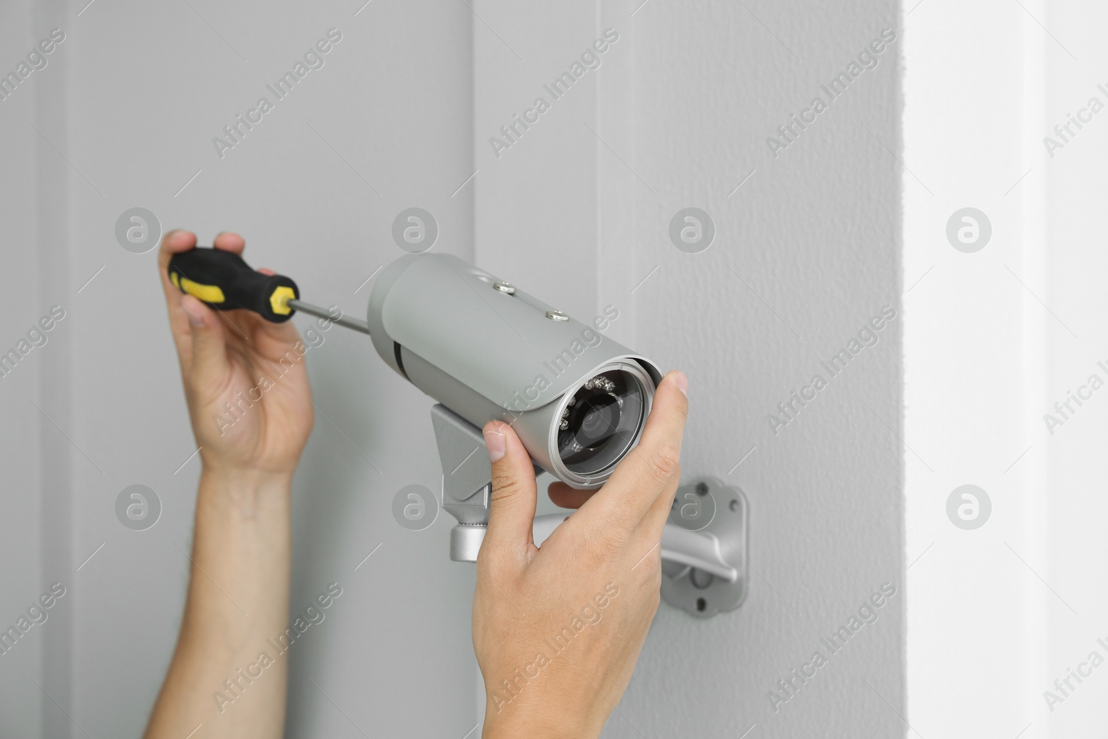 Photo of Technician with screwdriver installing CCTV camera on wall indoors, closeup