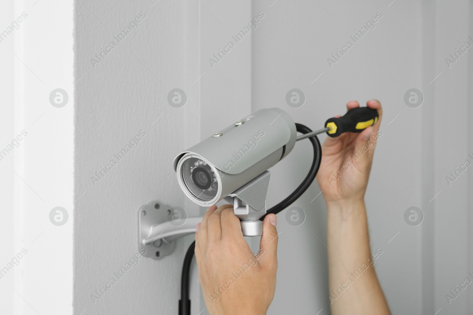 Photo of Technician with screwdriver installing CCTV camera on wall indoors, closeup