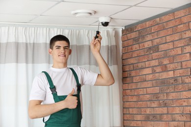 Technician showing thumbs up while installing CCTV camera with screwdriver on ceiling indoors
