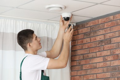 Photo of Technician with screwdriver installing CCTV camera on ceiling indoors