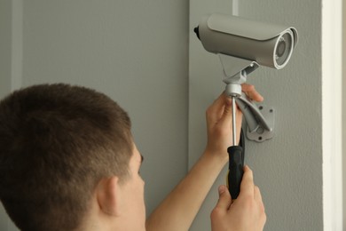 Photo of Technician with screwdriver installing CCTV camera on wall indoors, back view