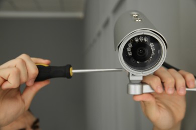 Technician with screwdriver installing CCTV camera on wall indoors, closeup