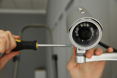 Photo of Technician with screwdriver installing CCTV camera on wall indoors, closeup