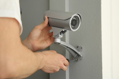 Photo of Technician with screwdriver installing CCTV camera on wall indoors, closeup