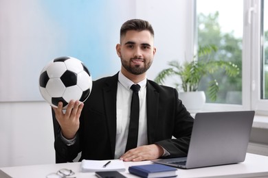 Young man with soccer ball at table in office