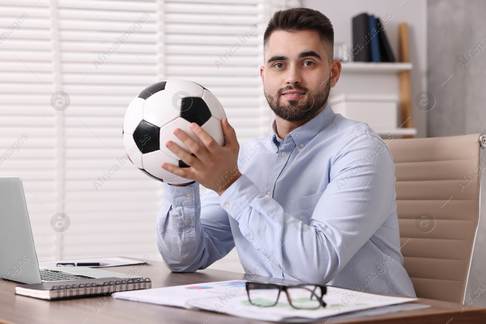 Photo of Young man with soccer ball at table in office