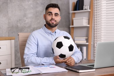 Photo of Young man with soccer ball at table in office