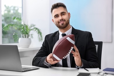 Young man with american football ball at table in office