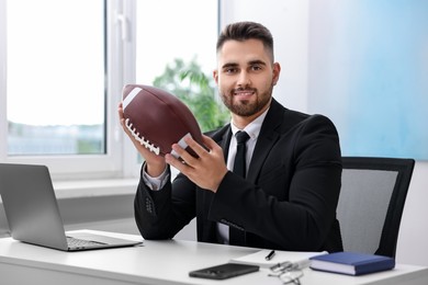 Young man with american football ball at table in office