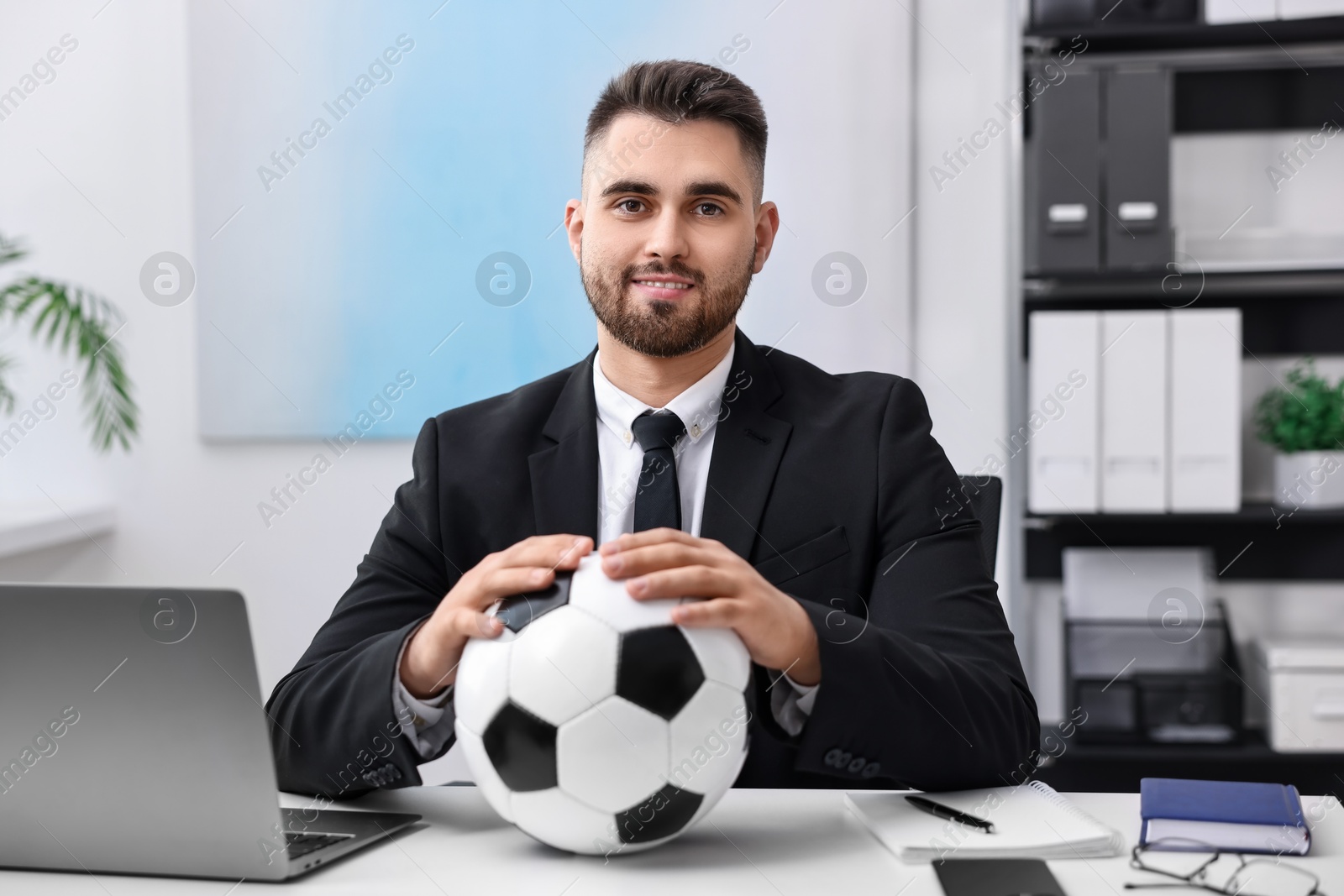 Photo of Young man with soccer ball at table in office