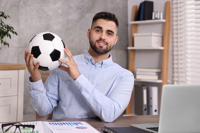 Photo of Young man with soccer ball at table in office