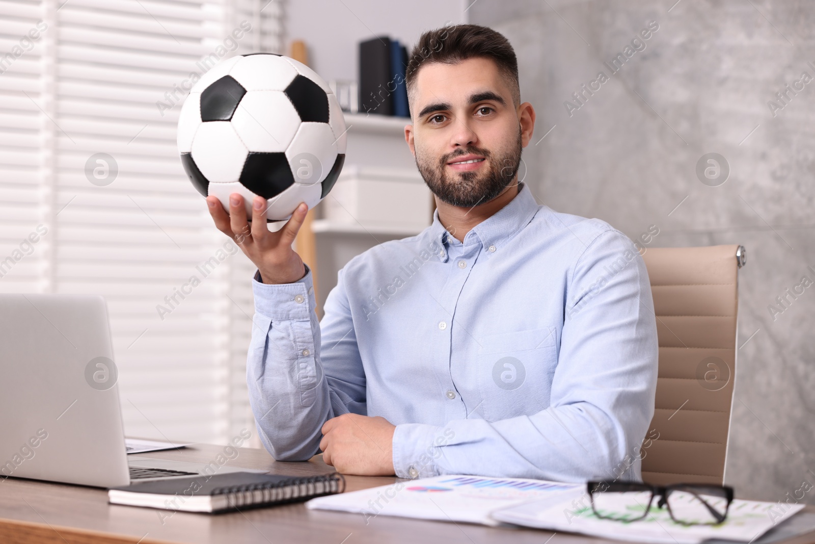 Photo of Young man with soccer ball at table in office